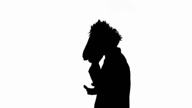 Black silhouette of man in business suit with horse head mask on white isolated studio background. Businessman walking and talking on smartphone. Concept of hard office work.