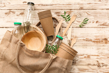Eco tableware with glass bottles, plant branches and bag on brown wooden background