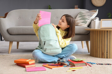 Little schoolgirl putting copybook in backpack at home