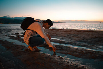Coastal Reflections: Kneeling Figure by Water's Edge at Sunset