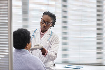 Waist up shot of African American female health practitioner holding patients face by chin during check up in clinic