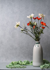 Red and white poppies in a light, tall vase. Still life, space for text