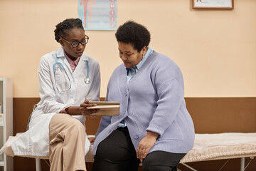 Medium long shot of African American woman doctor showing blood test result to mature female...