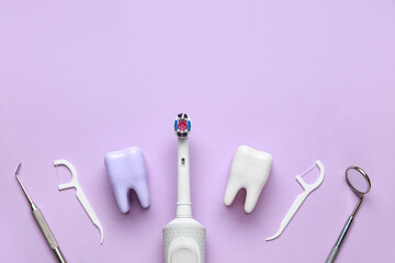 Plastic tooth models, electric toothbrush, floss toothpicks and dental tools on lilac background....