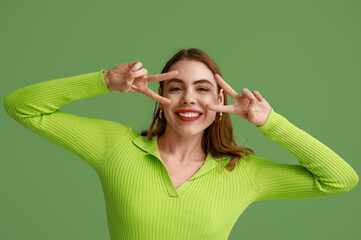 Pretty young woman showing peace gestures on green background