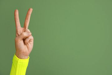 Female hand showing peace gesture on green background, closeup