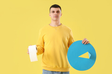 Young man with toilet paper and thumbtack on yellow background. Hemorrhoids concept