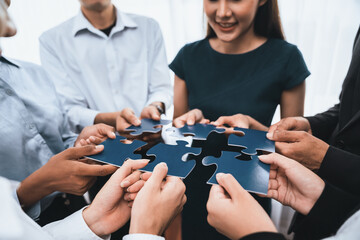 Diverse corporate officer workers collaborate in office, connecting puzzle pieces to represent partnership and teamwork. Unity and synergy in business concept by merging jigsaw puzzle. Concord
