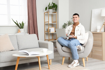 Young man using laptop in armchair at home