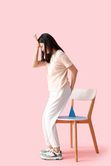 Young Asian woman with hemorrhoids and paper thumbtack on chair against pink background