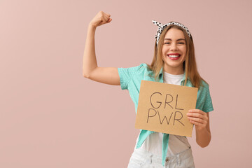 Happy young pin-up woman holding card with text GIRL POWER and showing her muscles on pink background