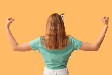 Pin-up woman showing her muscles on yellow background, back view