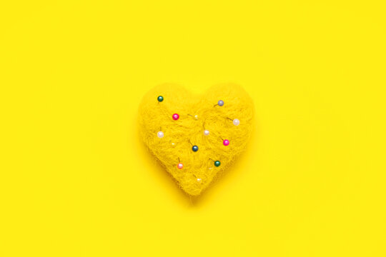 Heart-shaped pincushion with needles on yellow background. Valentine's day celebration