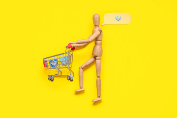 Creative composition with wooden mannequin and shopping cart on yellow background. Valentine's day...