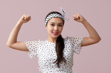 Beautiful young Asian pin-up woman showing her muscles on pink background
