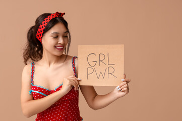 Beautiful young Asian pin-up woman holding card with text GIRL POWER on brown background