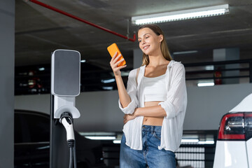 Young woman travel with EV electric car to shopping center parking lot charging in downtown city...