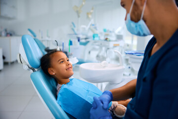 Happy black little girl talks to her dentist during teeth check-up.
