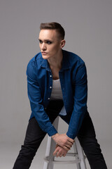 Fototapeta premium A young man in a blue shirt with the makeup of a rock musician sits on a bar stool.