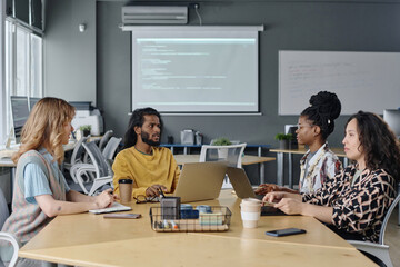 Indian office worker talking to his multi-ethnic female colleagues during their business meeting