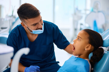 Happy dentist examining teeth of African American little girl at dental clinic.