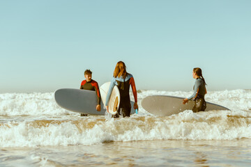 Group of surfers with surfboards in wetsuit entering towards ocean for ride the waves