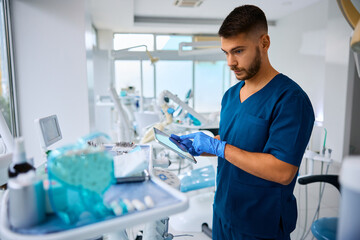 Obraz premium Pensive dentist working on digital tablet at dental clinic.