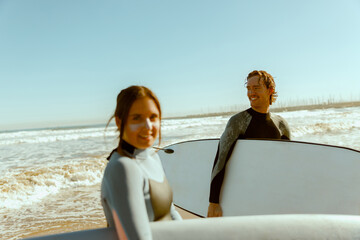 Two happy surfers in wetsuit with his surfboards entering out of sea after surfing on waves