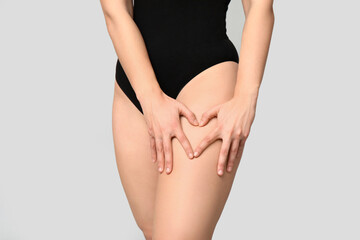 Body positive young woman making heart gesture on light background, closeup