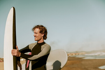 Male surfer in wetsuits standing with surfboard and preparing for ride on waves