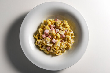 Top view of White soup bowl with tortellini with cream and ham