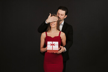 Attractive man closing her eyes and giving present isolated on black background. Couple in love...