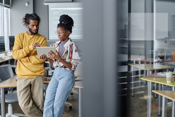Fototapeta premium Indian male office worker helping his african american female colleague with code on digital tablet