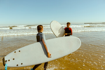 Couple of surfers in wetsuit with surfboards standing on the beach and looking each other