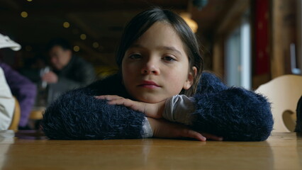 Closeup of 8 year old girl staring at camera with blank face expression, child daydreaming at diner