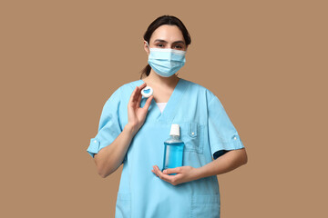 Young female dentist in mask with dental floss and mouth rinse on beige background