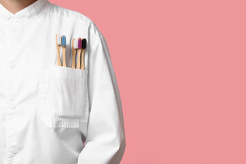 Female dentist with different toothbrushes in her pocket on pink background