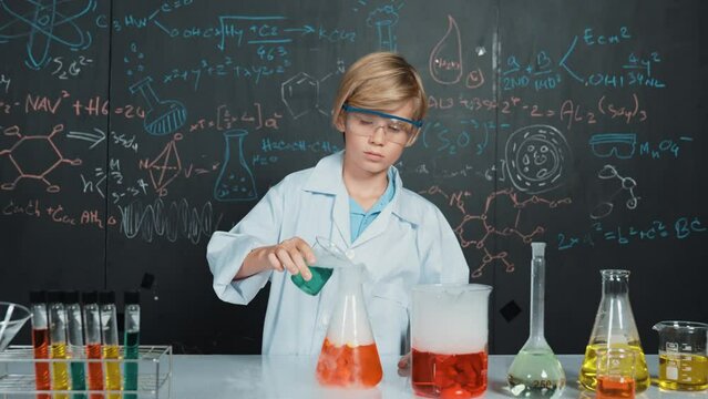 Smart boy inspect mixed chemical liquid in laboratory beakers while holding and looking carefully. Caucasian child focus on doing an experiment in chemistry lesson or STEM science class. Erudition.