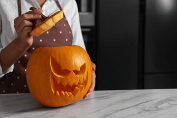 Woman with carved pumpkin for Halloween at white marble table in kitchen, closeup. Space for text