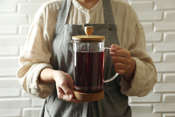 Woman holding teapot with freshly brewed hibiscus tea near white brick wall, closeup