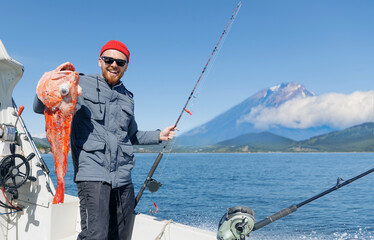 Happy Male fisherman holding red perch snapper big fish, Kamchatka Peninsula Russia. Deep sea sport...