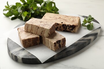 Pieces of tasty chocolate halva and mint on white marble table, closeup