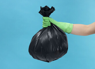 Woman holding plastic bag full of garbage on light blue background, closeup. Space for text