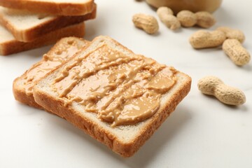 Delicious toasts with peanut butter and nuts on white table, closeup