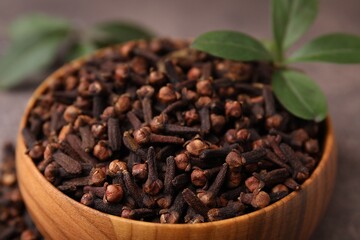 Aromatic cloves and green leaves in bowl on table, closeup