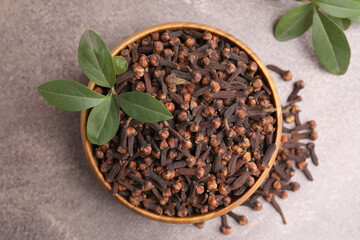 Aromatic cloves and green leaves in bowl on brown table, top view