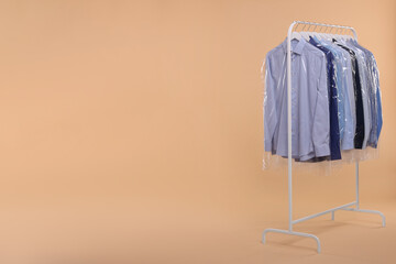 Dry-cleaning service. Many different clothes in plastic bags hanging on rack against beige background, space for text
