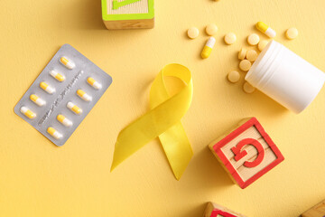 Golden ribbon with pills and toys on yellow background. Children cancer awareness concept