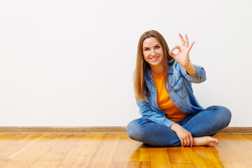 Happy Woman Sitting on Floor Showing OK Sign