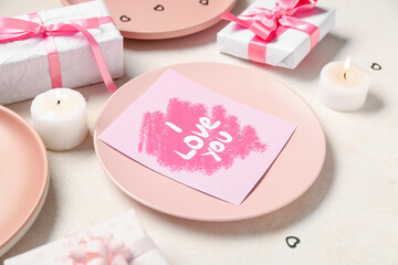 Beautiful table setting for Valentine's Day with festive card, gifts and candles on beige grunge background